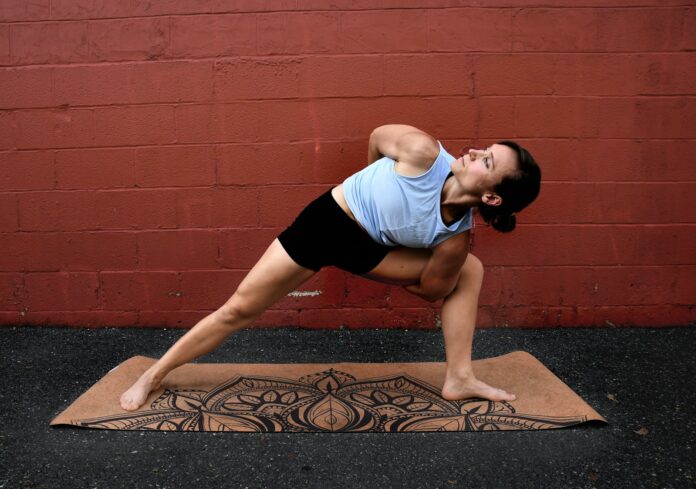 Photo by Natalie Runnerstrom woman in white tank top and black shorts doing yoga on brown concrete floor