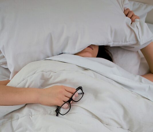 수면, 건강한 삶의 필수 열쇠… 올바른 수면 습관이 중요한 이유 person lying on bed while covering face with pillow and holding eyeglasses